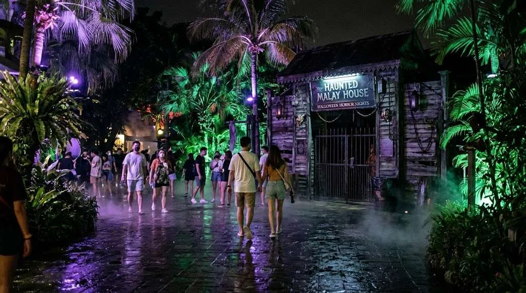 Visitors walking past the Haunted Malay House under tropical palm trees at Universal Studios Singapore Halloween Horror Nights