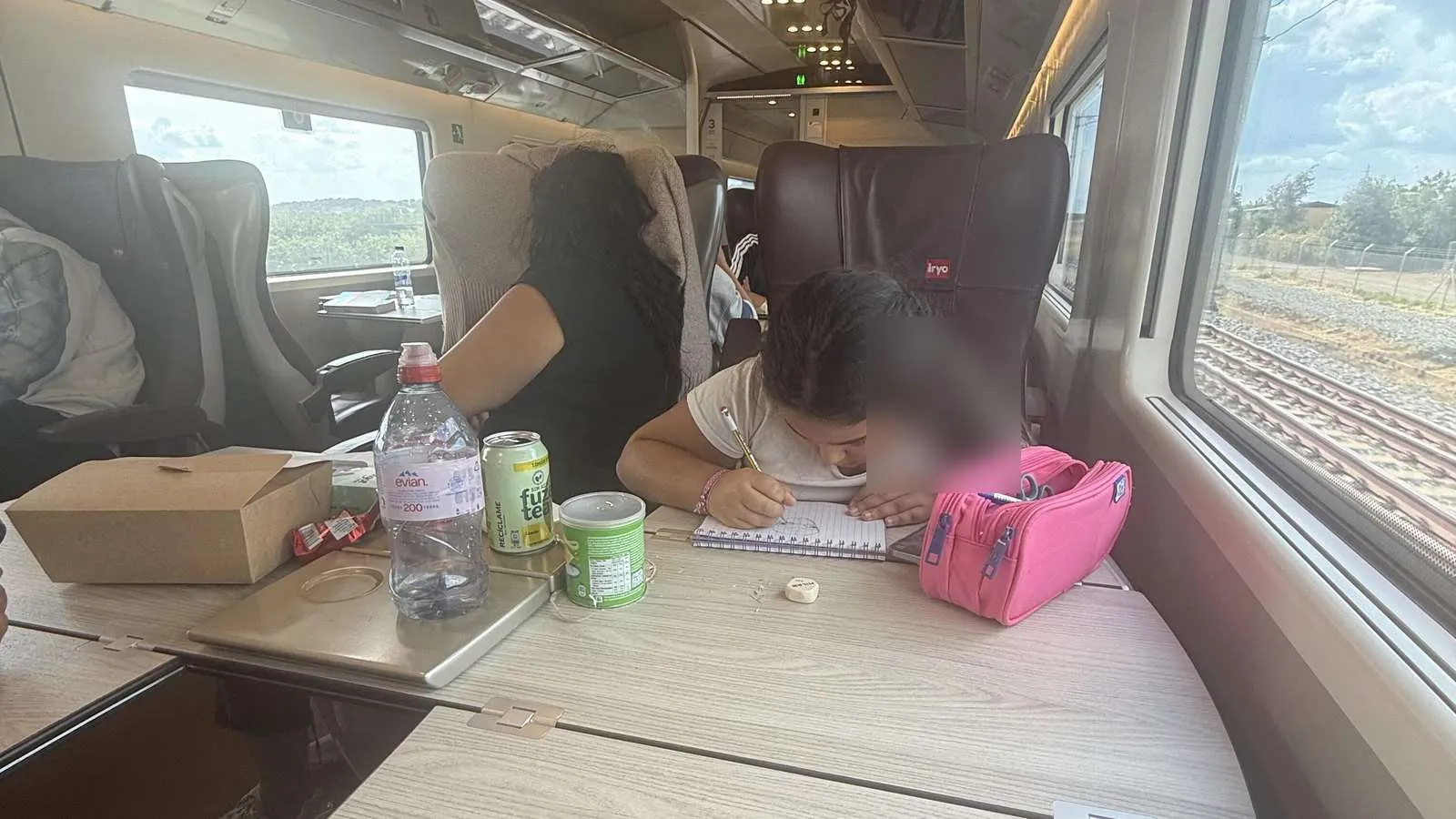 Table seats inside an iryo Infinita carriage, with a laptop, drinks and luggage space beside the window